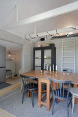 Dining table with chairs, fairy lights above, ladder to the lofted sleeping area and glass cabinet in the corner of the room