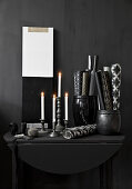 Brennende Kerzen und Papierrollen in Gefäßen auf schwarzem Konsolentisch