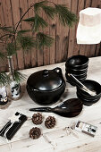 Black crockery and pine branches on table against rustic board wall