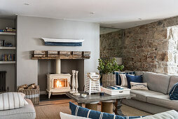 Wood stove in sitting room with exposed stone wall and mirrored alcove, a driftwood boat hangs above the fireplace