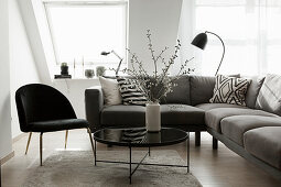 Grey sofa, black chair and coffee table with vase of branches