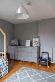 Graue Doppelkommode vor grauer Wand und kleiner Ledersessel im Kinderzimmer