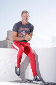 A grey-haired man wearing a t-shirt and red sports trousers