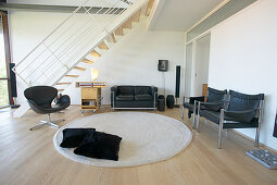 Black leather furniture, round rug and staircase in background of loft apartment