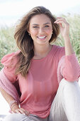 A young, long-haired woman wearing a pink blouse and light trousers