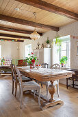 Solid wooded dining table in open-plan interior with wood-beamed ceiling