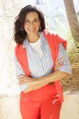 An older brunette woman wearing a blue-and-white striped shirt with a salmon-coloured jumper and trousers