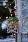 A lantern with Christmas decorations hanging on a window