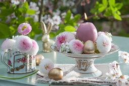 Romantische Osterdekoration mit Tausendschön, Gänsekresse und goldenen Ostereiern als Kerzenkranz