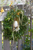 Boxwood Easter wreath decorated with Easter eggs and ribbon on the garden fence