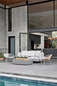 Outdoor furniture on terrace next to swimming pool outside two-storey house with glass walls