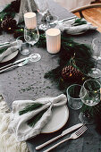 DIY-Girlande aus Kiefern- und Tannenzweigen mit verschiedenen Zapfen auf Weihnachtstisch, Gedeck mit Kiefer-Tasseln als Serviettenringe