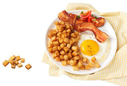American breakfast with hashbrowns, bacon, pork, meat, tomatoes, and eggs sunny side up