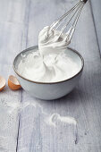 Whipped egg whites (meringue) in a bowl and on a whisk