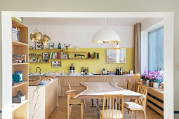 Designertisch aus hellem Holz in offener Küche mit gelber Wand