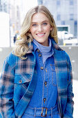 A young blonde woman wearing blue denim dungarees and a checked jacket