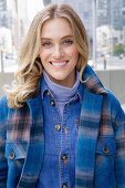 A young blonde woman wearing blue denim dungarees and a checked jacket