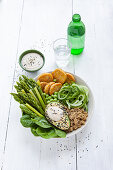 Healthy green bowl with green asparagus, tempeh, quinoa, and tahini dipping sauce