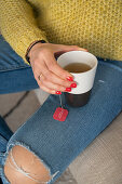 Frauenhand hält Becher mit Tee und Teebeutel