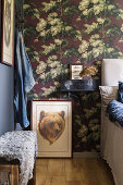Picture with brown bear head next to a bed in bedroom with floral wallpaper