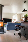 Kitchen counter with bar stools, wood stove, upholstered sofa and TV in open-plan living room