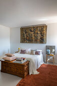 Tapestry above a queen size bed and antique wooden chest in bedroom