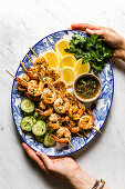 Grilled Shrimp skewers served on a blue ceramic plate with lemon and cucumber