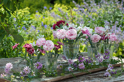 Small bouquets of carnation blossoms and candles as table decoration placed on a board and decorated with tendrils of crownvetch