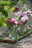 Kleine Sträuße aus Nelkenblüten und Prachtkerzen als Tischdeko auf ein Brett gestellt und mit Ranken von Kronwicke dekoriert