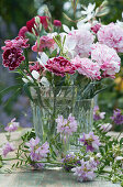 Small bouquet of carnation blossoms and magnificent candle, tendrils of crown vetch in front of it