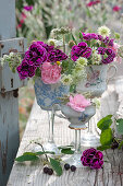 Unusual decoration idea with carnations, widow flowers and wild carrot in cups on glass base, branch of rock pear