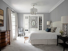 Double bed and antique chest of drawers in bedroom with light grey walls