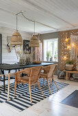 Dining table with rattan armchairs on black and white carpet, above boho hanging pendant light