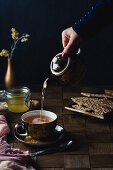 Womans hand pouring hot ginger tea in a tea cup