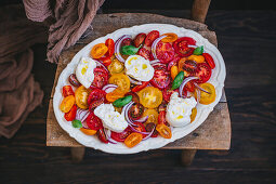 Colourful Caprese salad served on a large plate, rustic chair