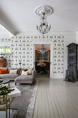 Sofa and wood-burning stove in open-plan living room with patterned wallpaper and pale floorboards