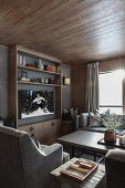 Grey upholstered furniture, coffee table and shelf in room with grey wall and wooden ceiling