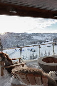 Blick vom Balkon mit Outdoor-Sesseln und Glasbalustrade auf schneebedeckte Landschaft