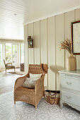 Wicker chair, tiled floor and panelled walls in hallway decorated in natural shades