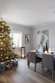 Beleuchteter Weihnachtsbaum, darunter Geschenke und festlich gedeckter Esstisch im Zimmer