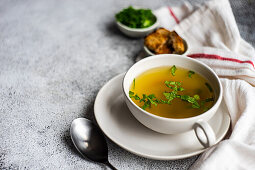 Chicken broth served in a bowl and set with fresh green onion and fried bread