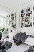 Weißes Wohnzimmer mit Regalwand, Sofa und Spiegelwand