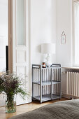 Glasvase mit Gartenblumen und Regal mit weißer Tischlampe in minimalistischem Schlafzimmer