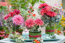 Sträuße mit Dahlien und Hortensienblüten in mit Blättern umwickelten Gläsern