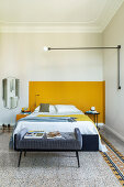 Gepolsterte Kleiderbank und Doppelbett vor gelber Wand im Schlafzimmer