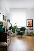 Seating area with green armchair and houseplant next to window with wooden cabinet in foreground