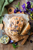 Bread with viola blossoms on a wooden cutting board next to cheese spread