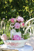 Pfingstrosenstrauß in nostalgischer Vase auf Gartentisch