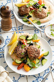 Herb turkey patties on a pita with fresh vegetables, lemon and olives