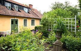 Urn on a stone plinth and trellis in the spring garden in front of the house